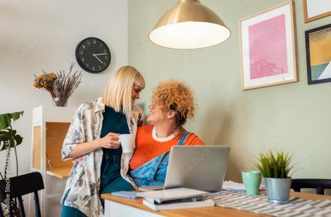 Twee vrouwen lachen naar en omhelzen elkaar op een stoel aan tafel.