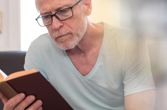 Portret van oudere blanke man met bril en witte snor en baard die een boek leest, lichteffect.