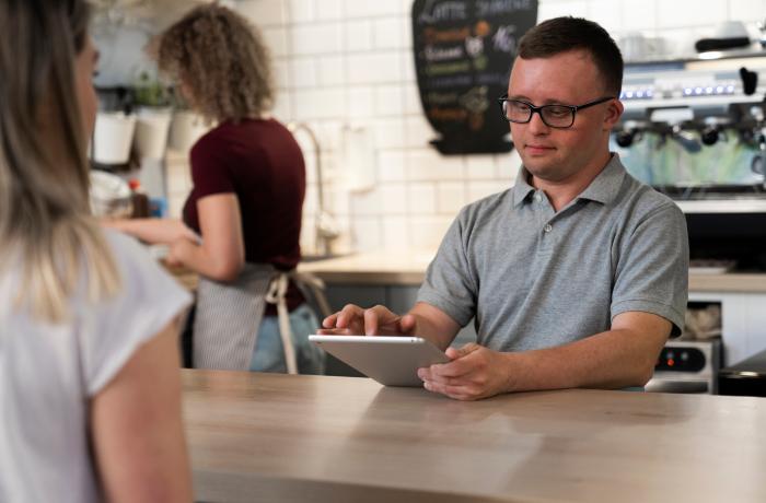 Kaukasische man met het syndroom van Down neemt bestelling op in het café met behulp van een digitale tablet.