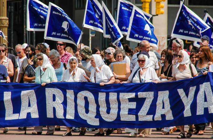 Protestoptocht met vlaggen en banner; de moeders van Plaza de Mayo eisen gerechtigheid in de naam van en de waarheid over hun vermiste zonen en dochters.