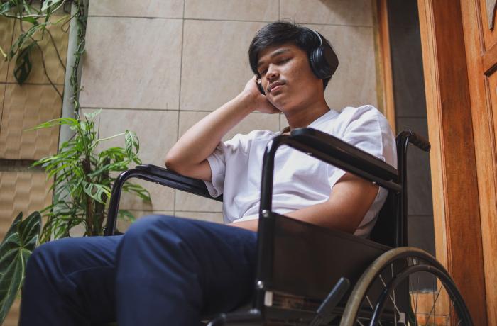 jongen luistert thuis naar muziek via hoofdtelefoon, in een rolstoel