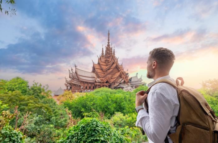 Man met rugzak kijkt naar tempel in de verte tegen vredige avondlucht (pastelkleuren roos en blauw)